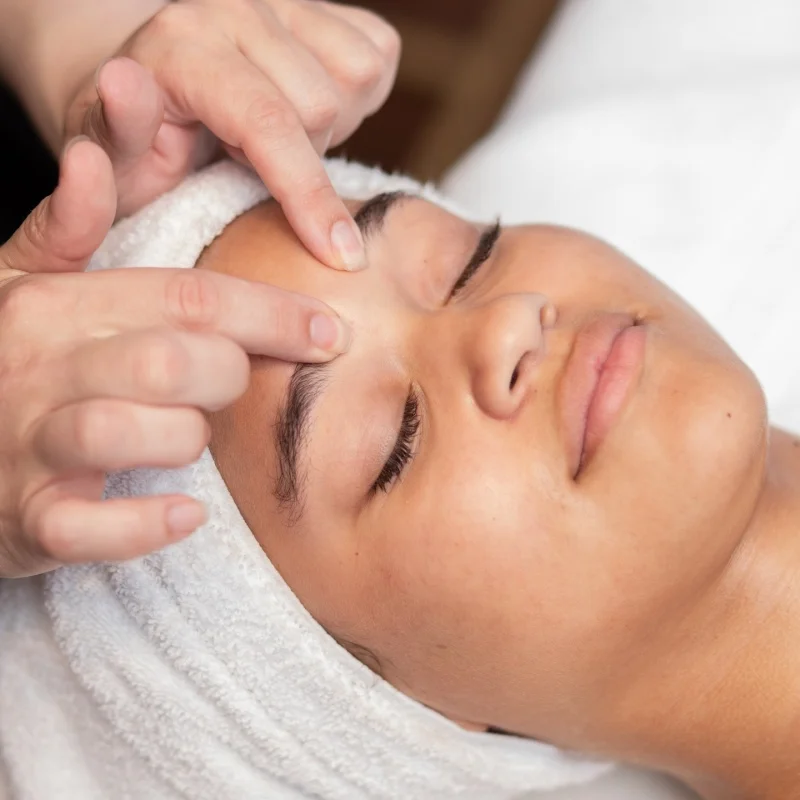 Fingers press against a young woman's forehead during the extraction process of a facial