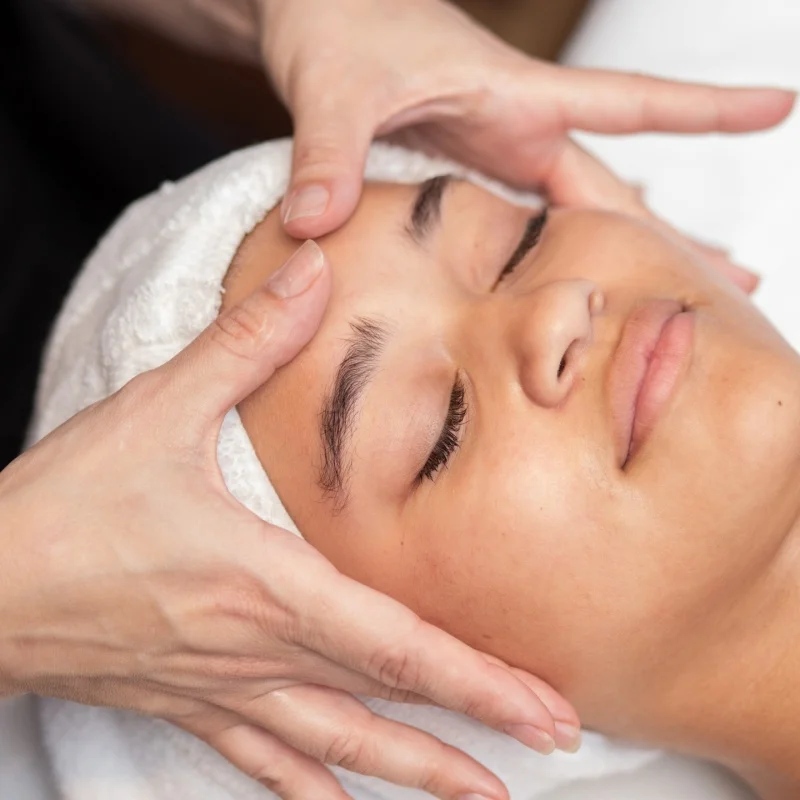 Fingers apply pressure to a young woman's forehead during a facial treatment