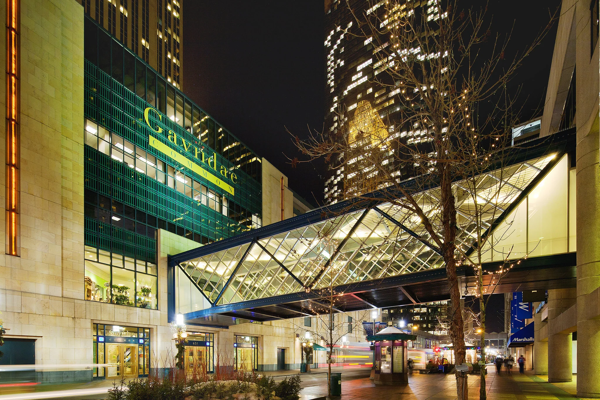 A skyway connects to a large shopping center during nightfall.