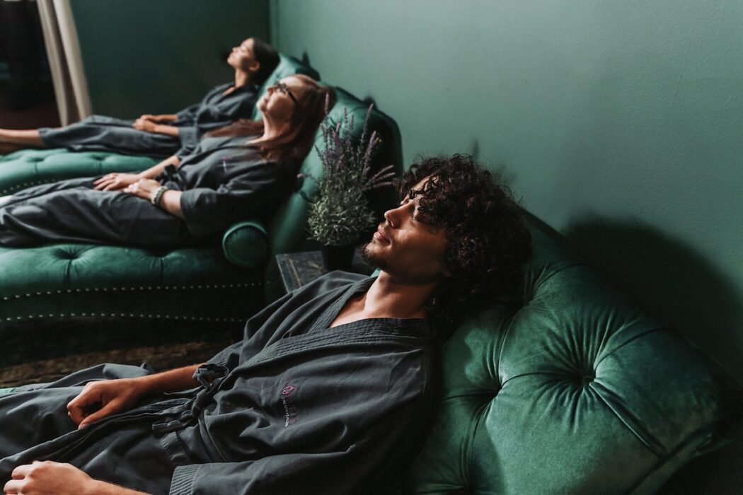 A man and two women relax in green lounge chairs in their spa bathing robes